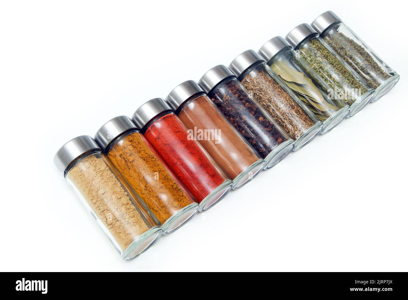 The different types of spices and herbs stored inside the small closable glass bottle isolated on a white background. Stock Photo
