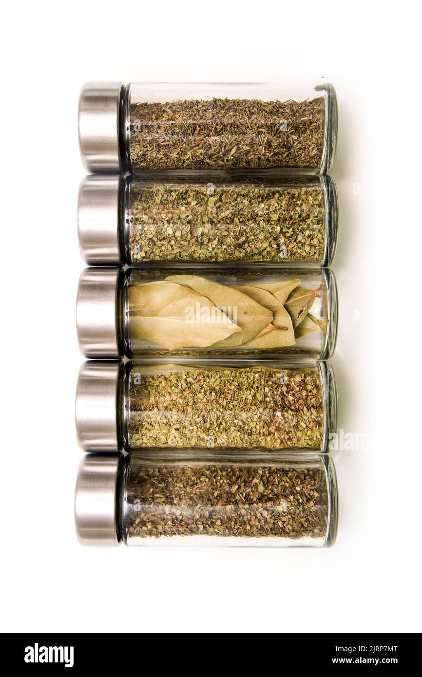 The different types of spices and herbs stored inside the small closable glass bottle isolated on a white background. Stock Photo