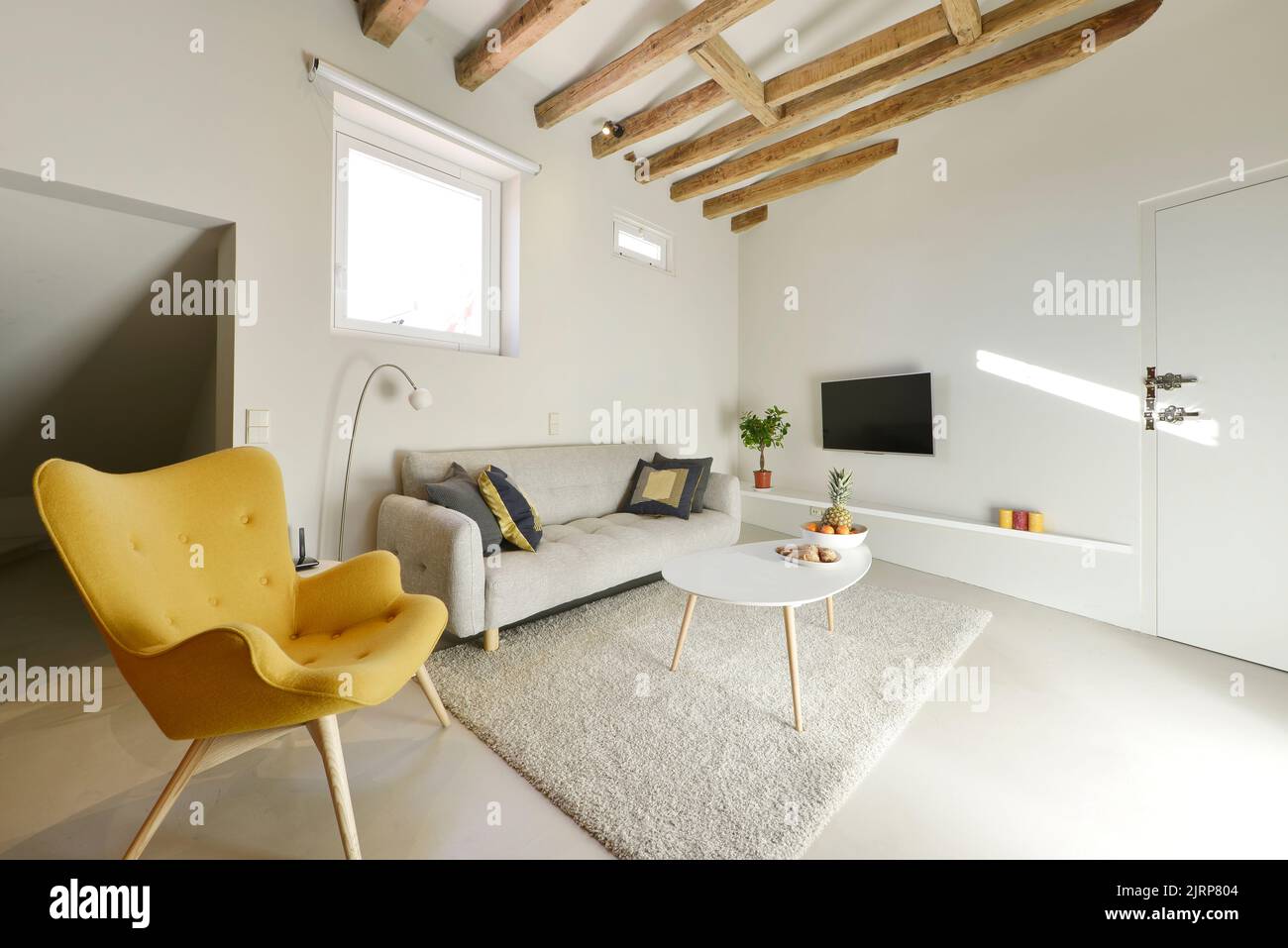Living room with gray three-seater sofa and yellow wing-back sofa and sloping ceilings with wooden Stock Photo