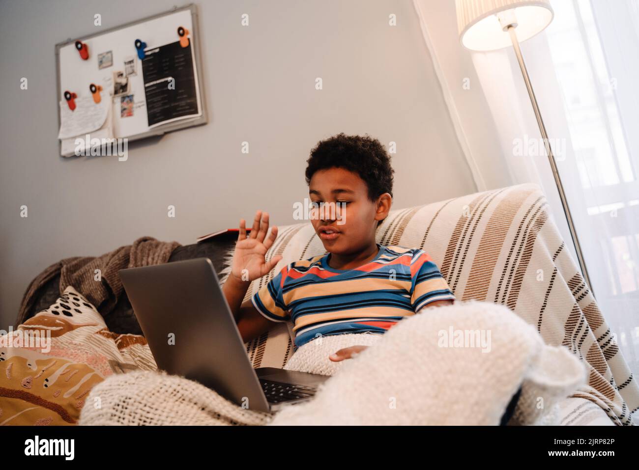 Black boy gesturing and using laptop while sitting on sofa at home Stock Photo