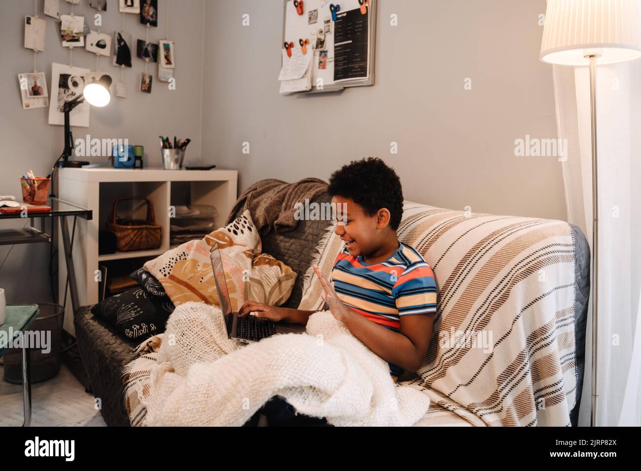 Black boy gesturing and using laptop while sitting on sofa at home Stock Photo