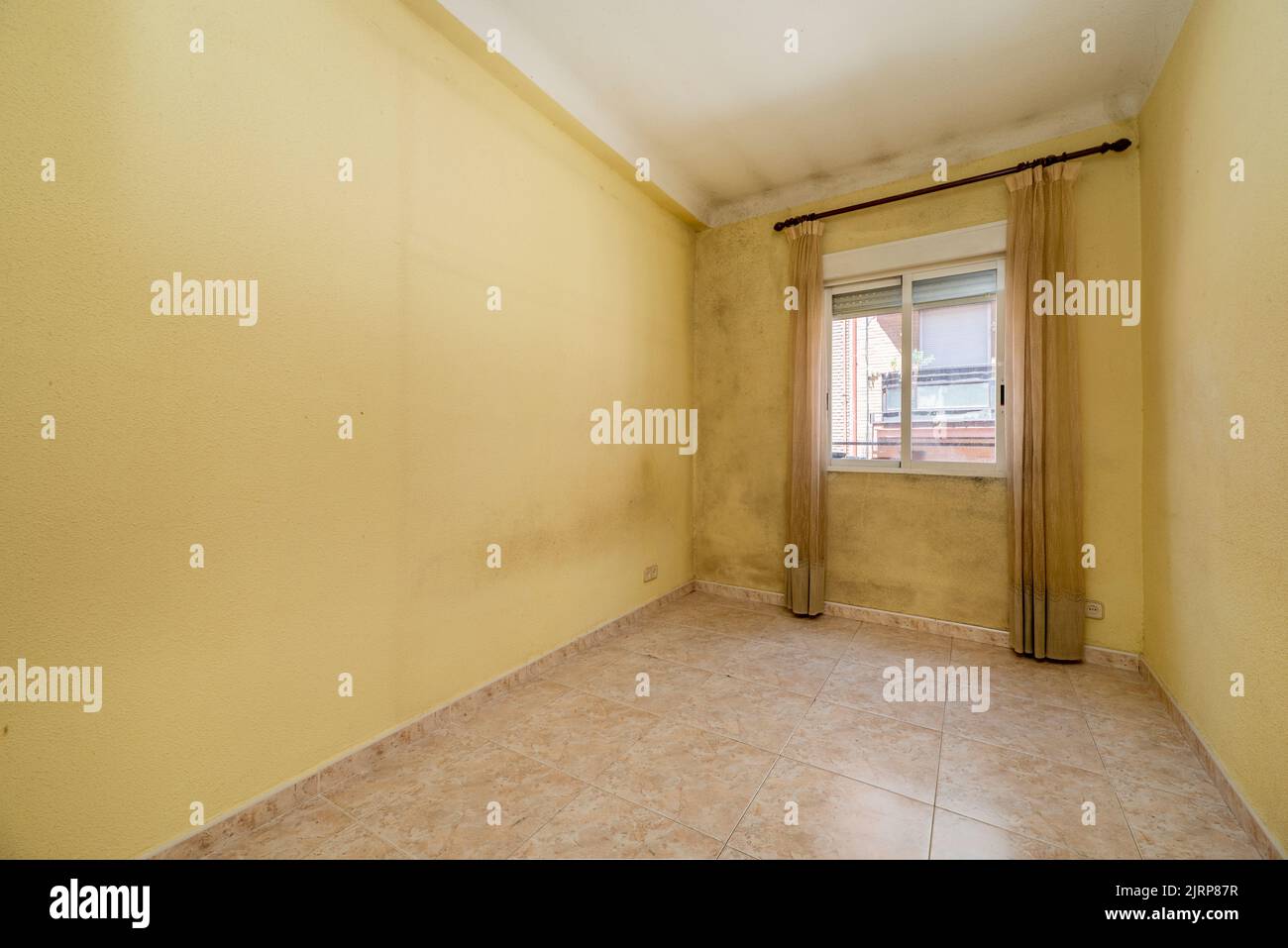 Empty room with yellow painted walls and a dirty one with curtains and pink stoneware floors Stock Photo