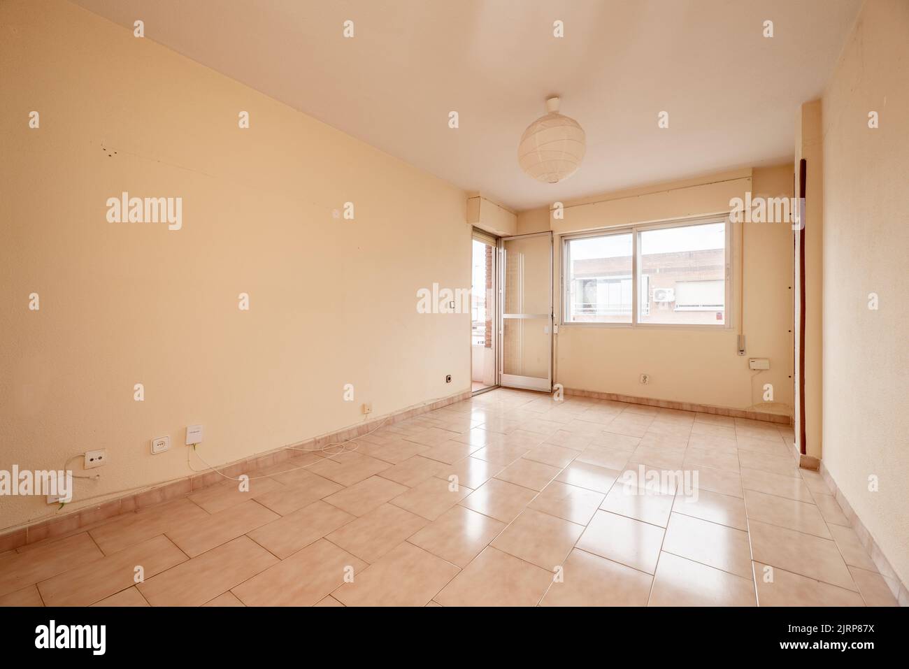 Empty room with pale pink painted walls and stoneware floors of the same color with windows and access to a terrace Stock Photo