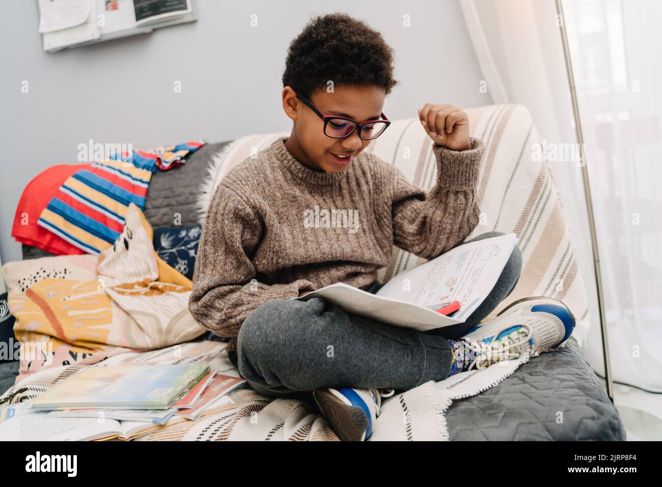 Black boy using mobile phone and doing homework on sofa at home Stock Photo