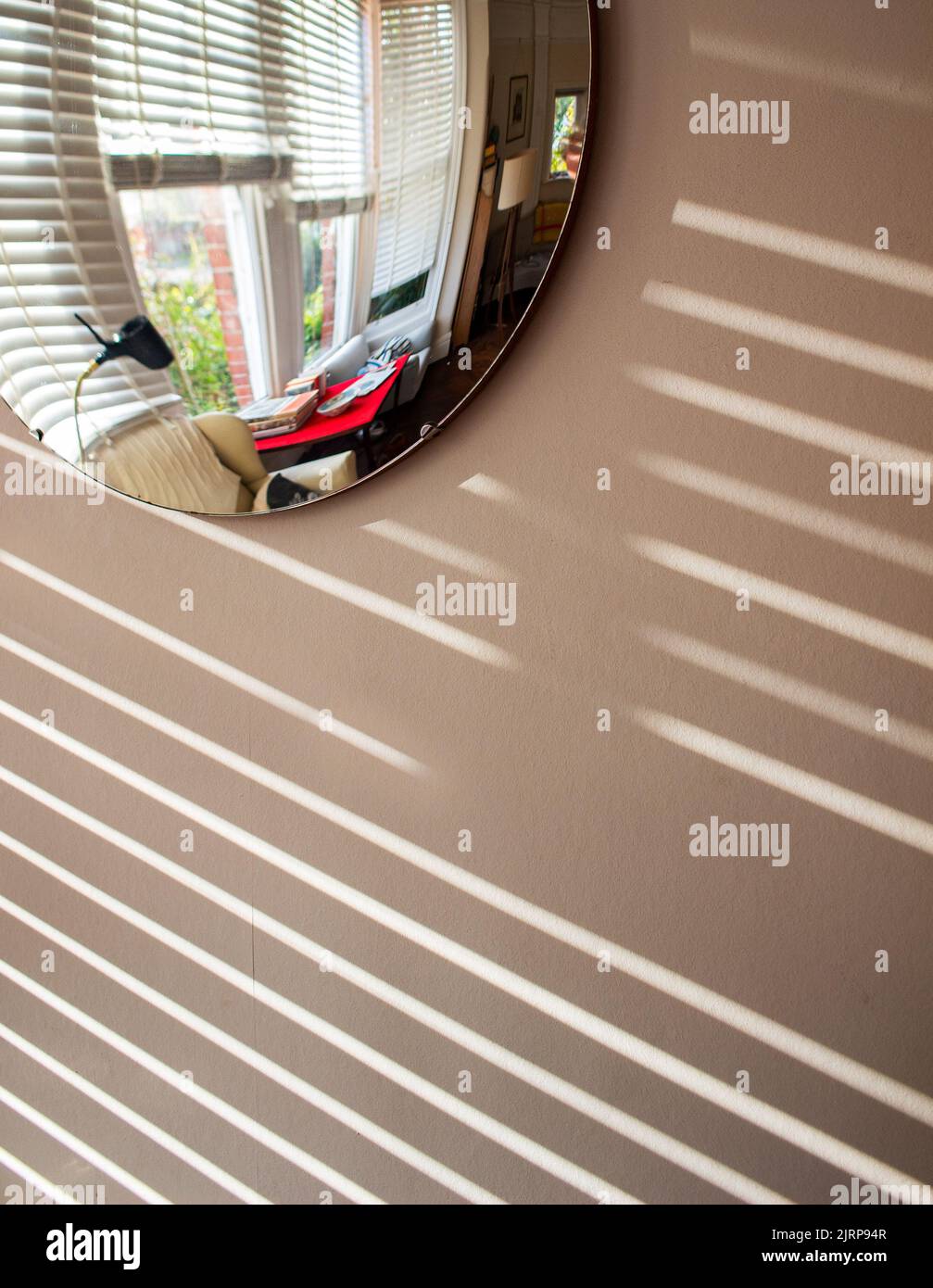 A convex mirror hanging on a wall in Sussex, in afternoon sunlight, barred shadows through Venetian blinds Stock Photo