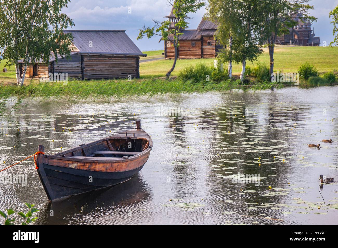 Landscape on Kizhi island in Lake Onega on a summer sunny day. Old wooden fishing boat Kizhanka on shore. Village with vintage mill, temple and church Stock Photo