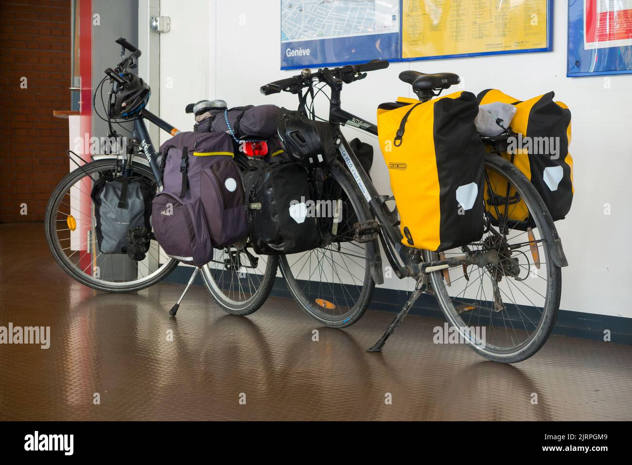 Two touring bicycles, heavily laden with cycle / bike panniers, left standing by their cycle riding owners at a train station on the French and Swiss border between France Switzerland. (131) Stock Photo