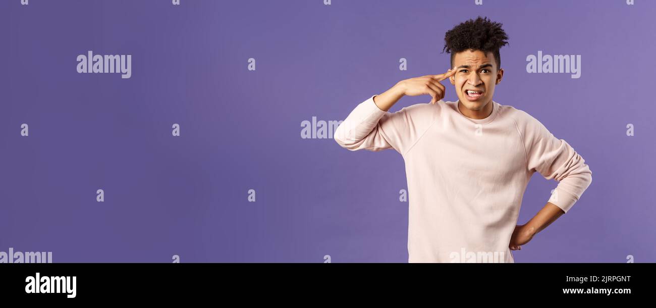 Portrait of angry, annoyed young man scolding someone from being stupid and crazy, rolling index finger over temple staring outraged and irritated Stock Photo