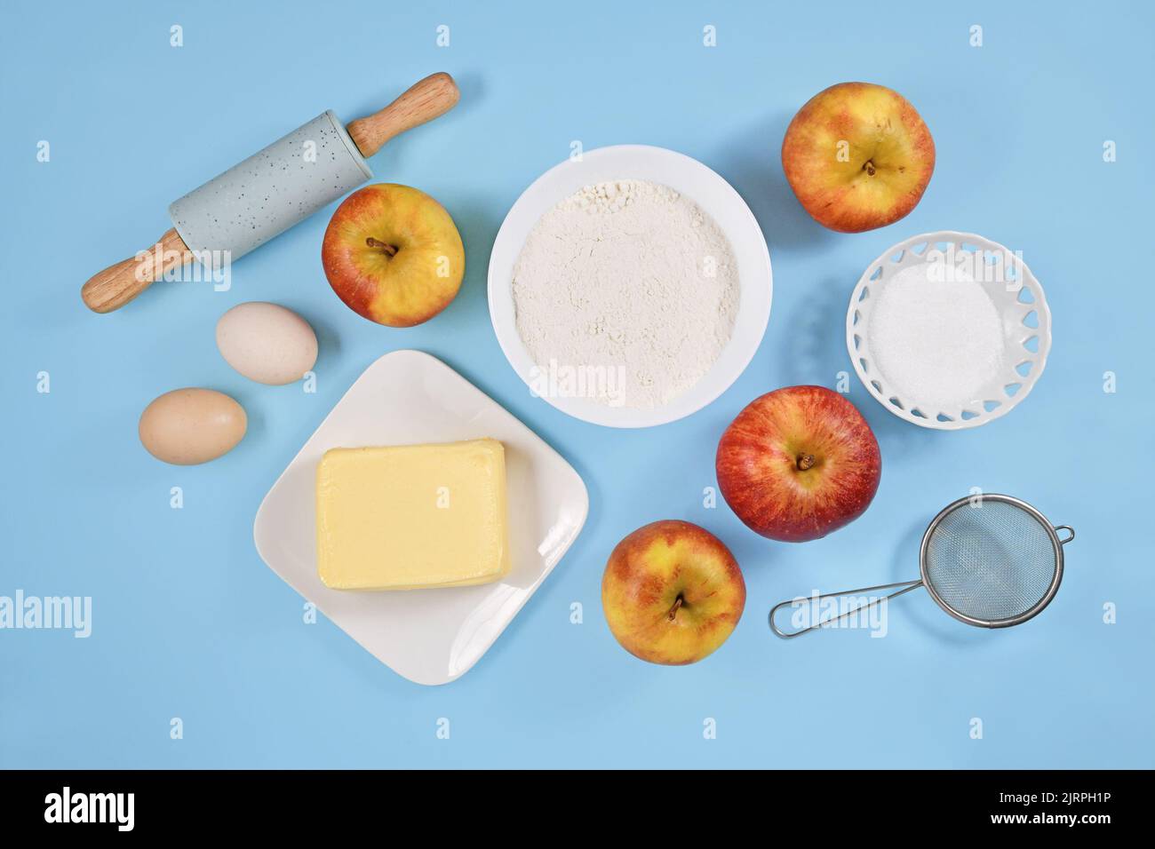 Baking ingredients for apple pie with butter, flour, sugar, eggs and fruits on blue background Stock Photo