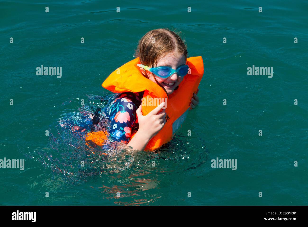 Young girl / kid / child aged eight years swimming in water / learning