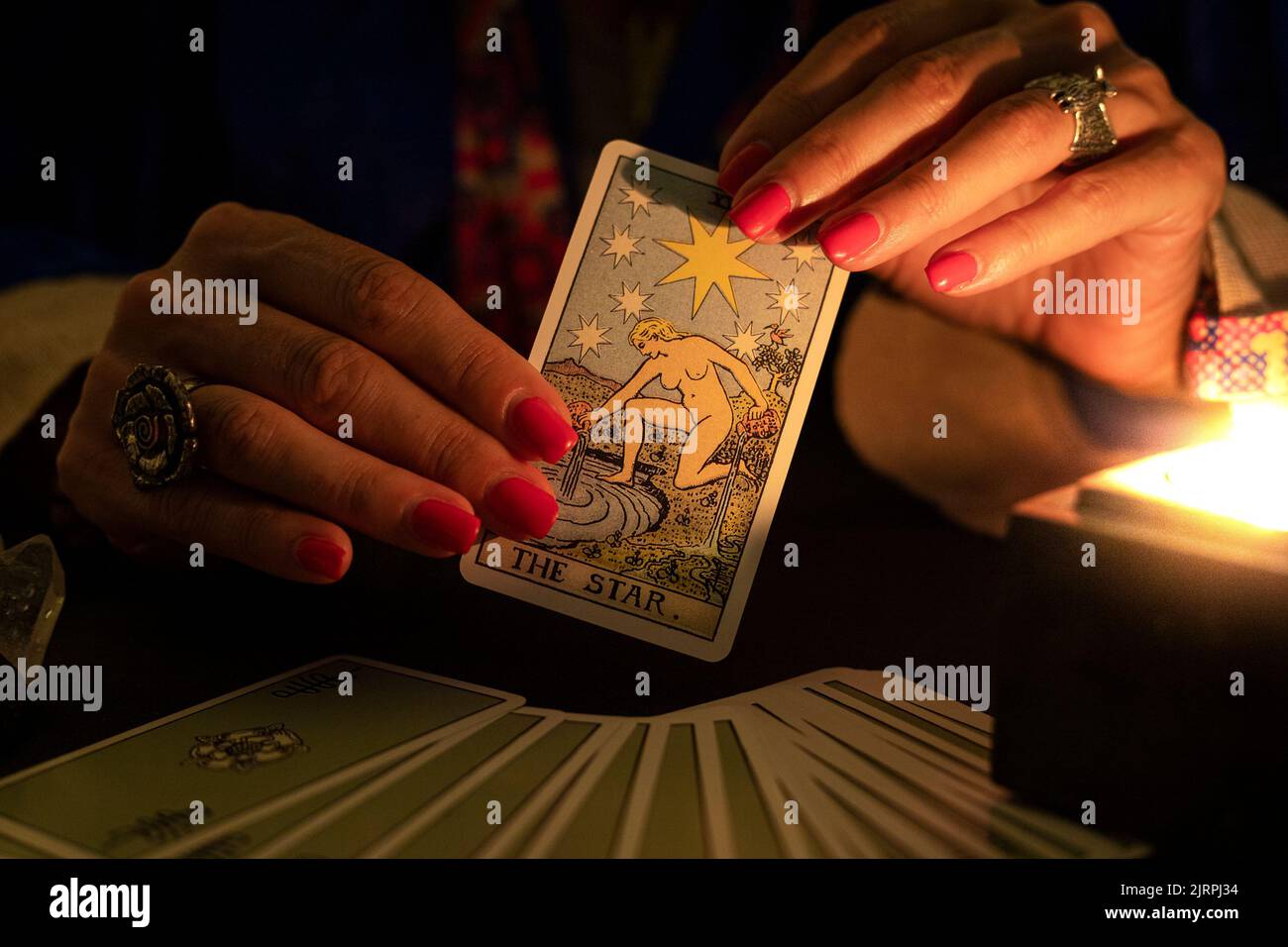 Fortune teller female hands showing The Star tarot card, symbol of hope, during a reading. Close-up with candle light, moody atmosphere. Stock Photo