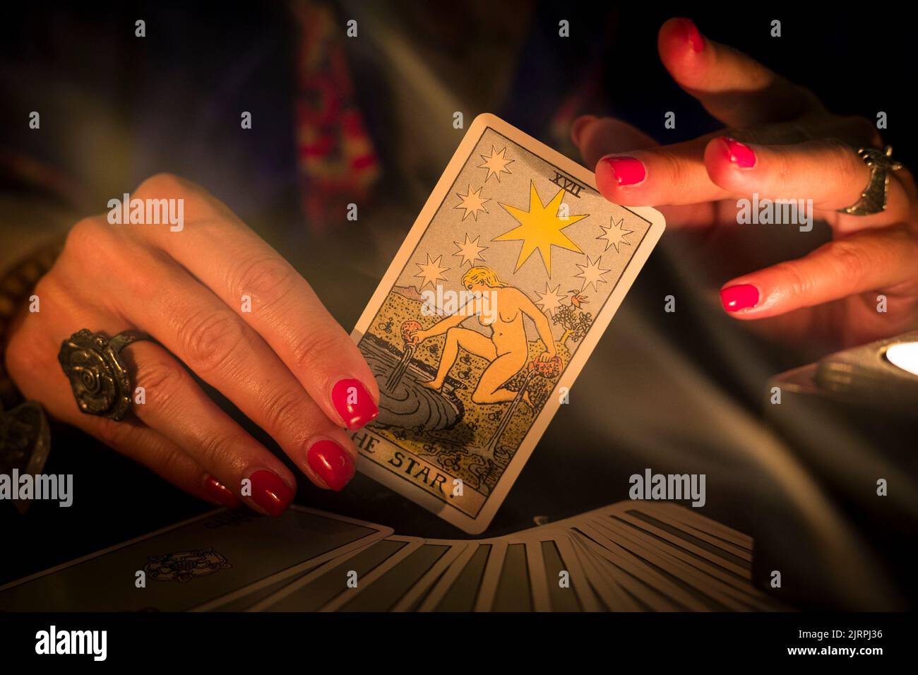 Fortune teller female hands showing The Star tarot card, symbol of hope, during a reading. Close-up with candle light and smoke, moody atmosphere. Stock Photo