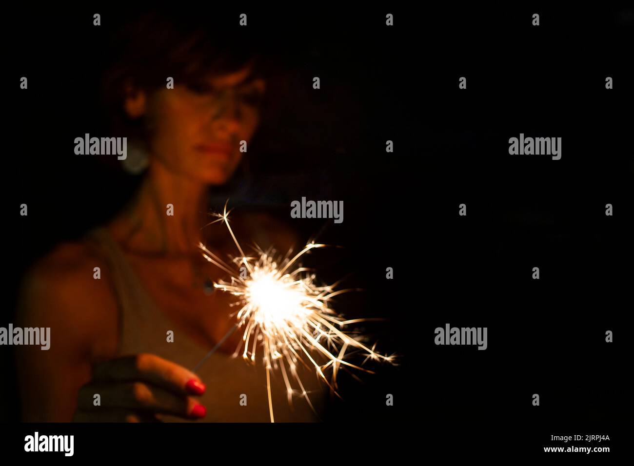 Attractive  caucasian woman, blurred face, holding a burning sparkler or bengal in the dark. Copy space. Holidays or magic background or wallpaper. Stock Photo