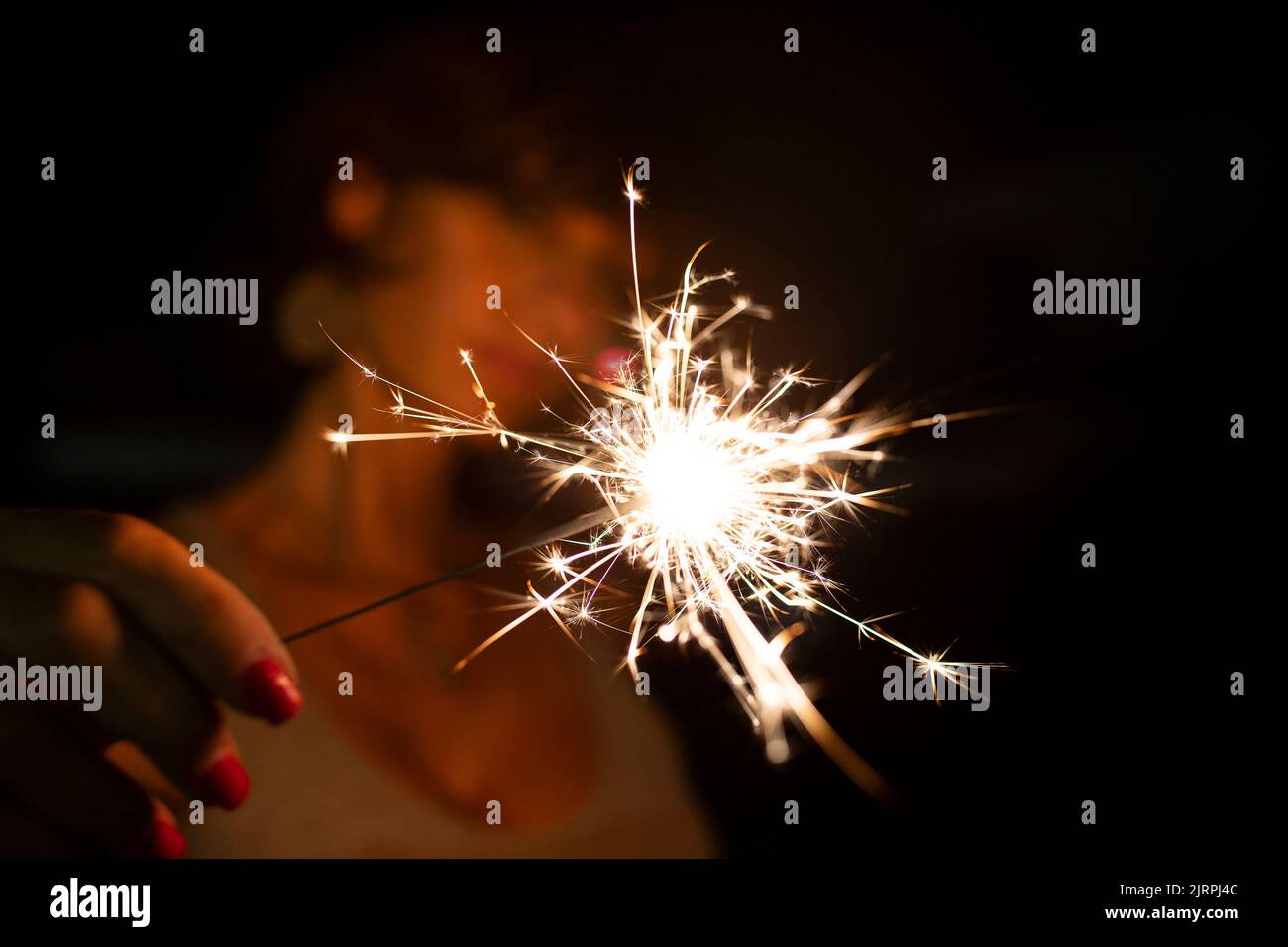 Attractive caucasian woman, blurred face, holding a burning sparkler or bengal in the dark. Copy space. Holidays or magic background or wallpaper. Stock Photo