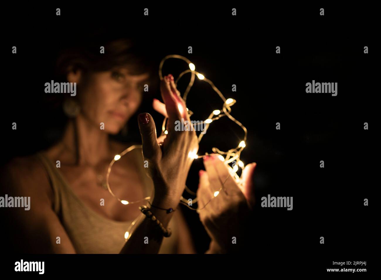Beautiful caucasian woman, blurred face, holding string lights in the dark. Copy space. Holidays or magic background or wallpaper. Stock Photo