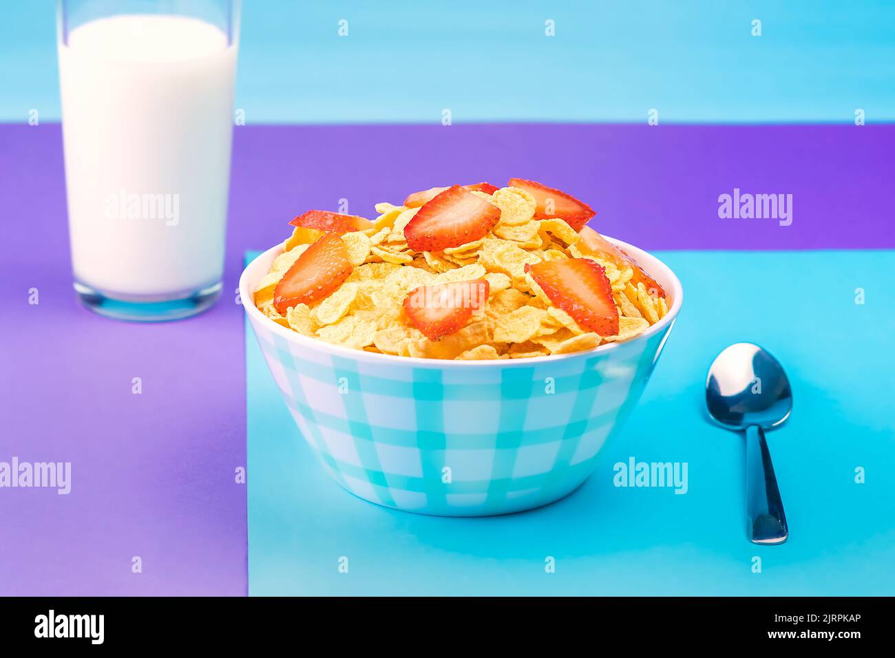 View of a plate with natural cereal and red strawberries with a glass of fresh milk against a background of pastel colors. Stock Photo