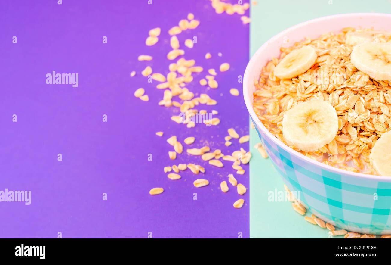 Zoom in on a plate of plain oatmeal with bananas and a glass of fresh milk against a background of pastel colors, ready to copy space for breakfast. Stock Photo