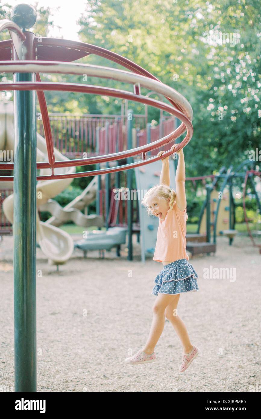 Four year old blonde girl hangs from playground equipment in Maryland Stock Photo