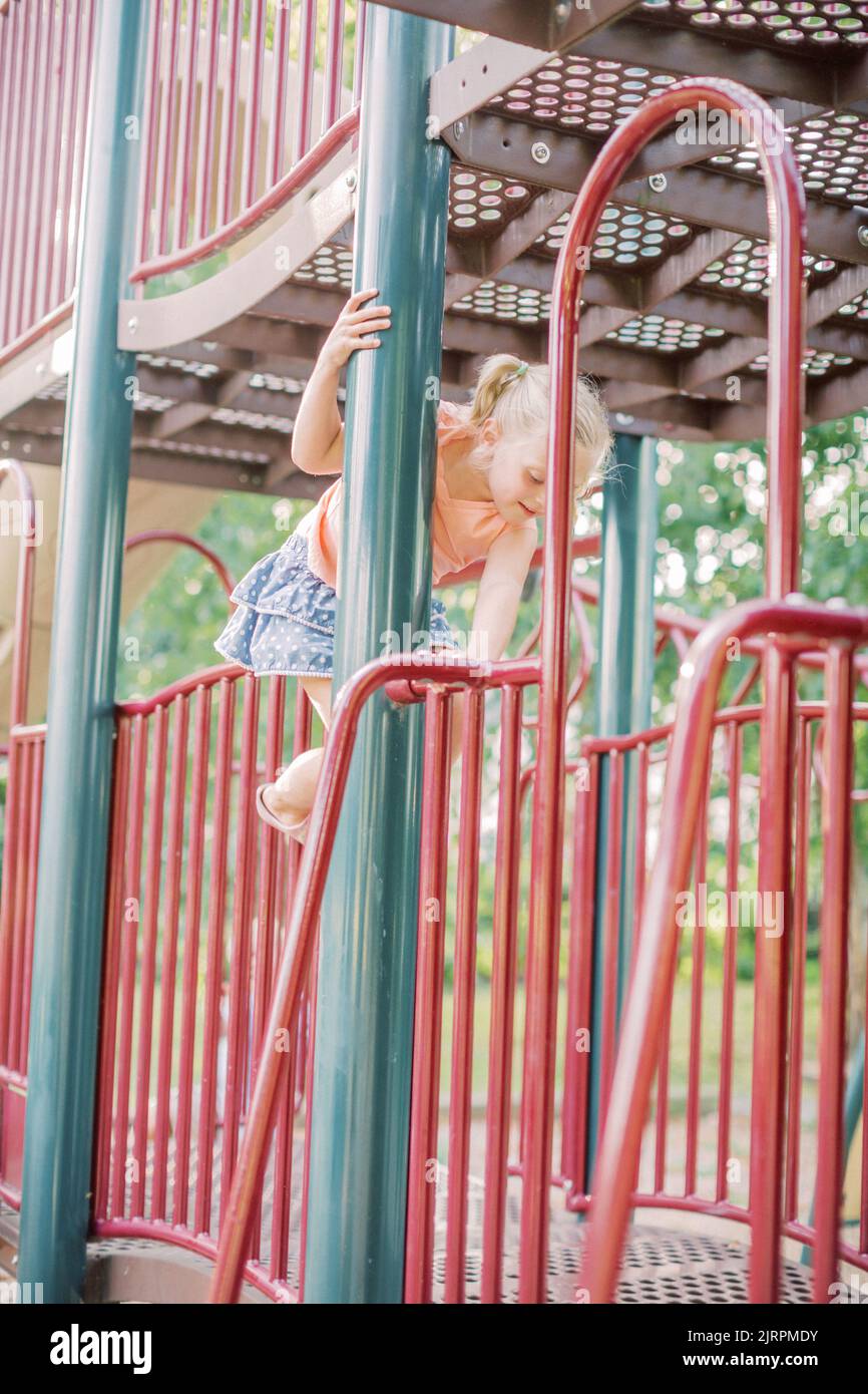 4-5-year-old Caucasian girl climbs playground equipment. Stock Photo