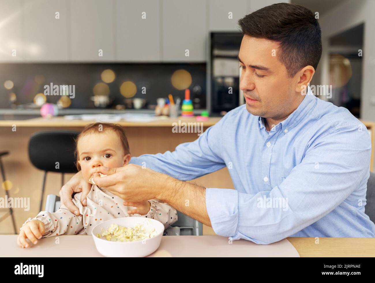 middle-aged father feeding baby daughter at home Stock Photo