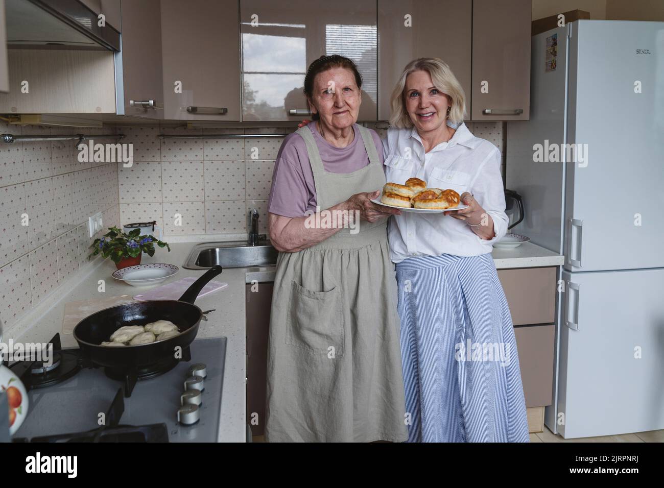 An aged mother and daughter are cooking pies in the kitchen. Stock Photo