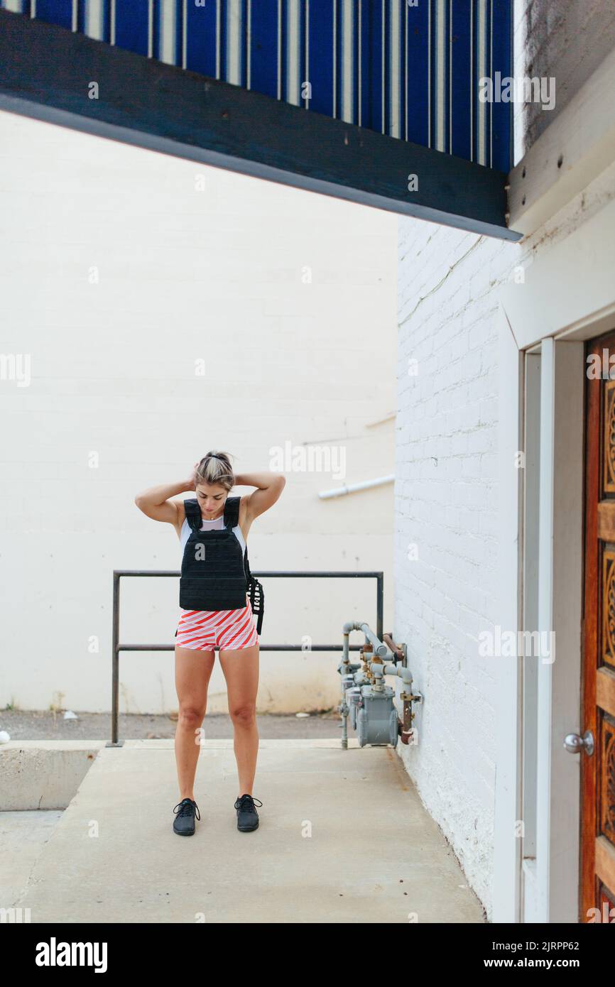 Fitness woman doing squats outside wearing weighted vest in fron Stock