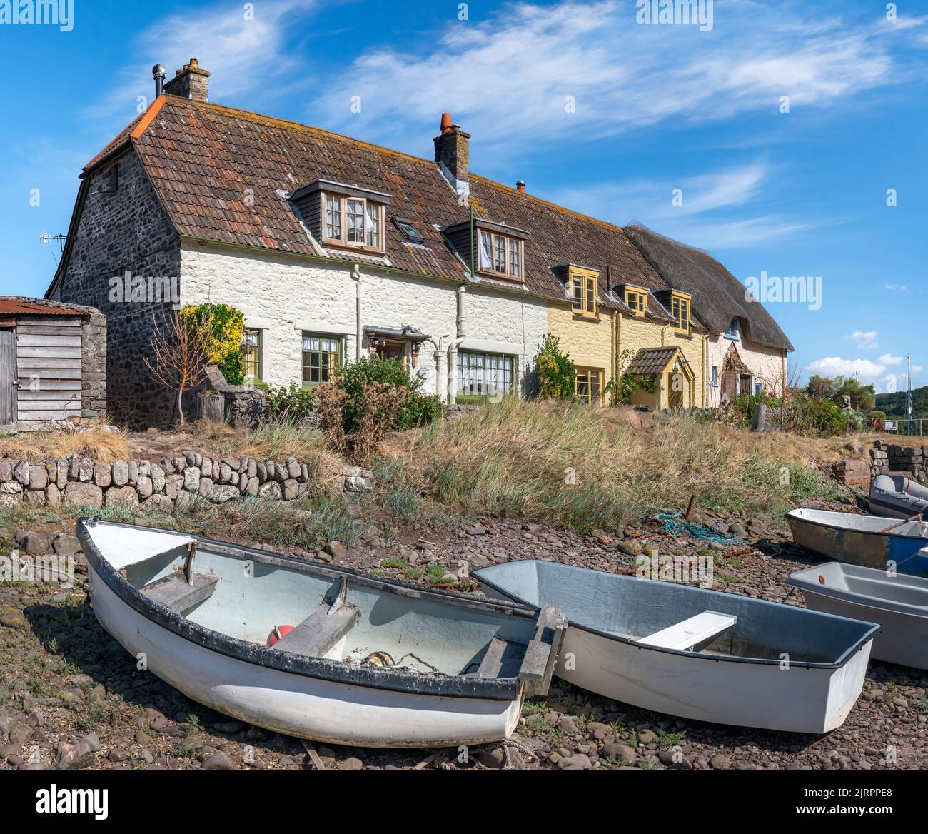 At low tide a row of small boats lie on the shingle in font of the small cottages at Porlock Weir in Somerset. Stock Photo