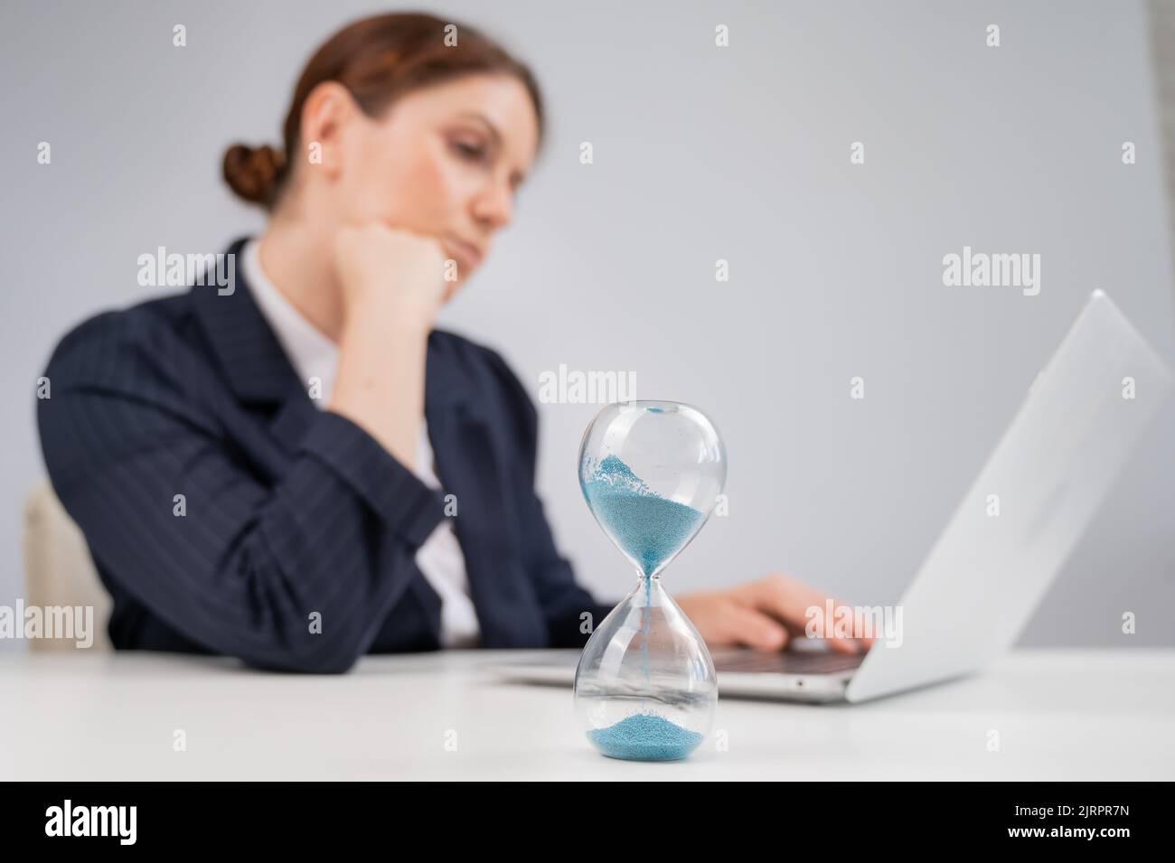 Business woman keeps track of time on an hourglass while working Stock