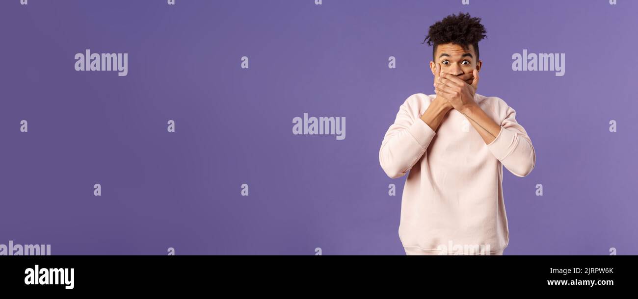 Portrait of shocked impressed young hispanic man found out gossip, heard rumour, trying not laugh shut his mouth with hands and express amazement and Stock Photo