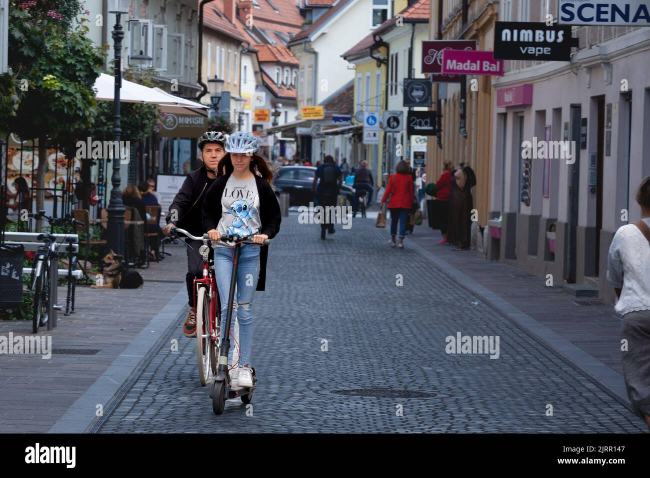 Picture of a girlstanding in a street of Ljubljana riding electric scooters in a pedestrian alley in Slovenia. Stock Photo