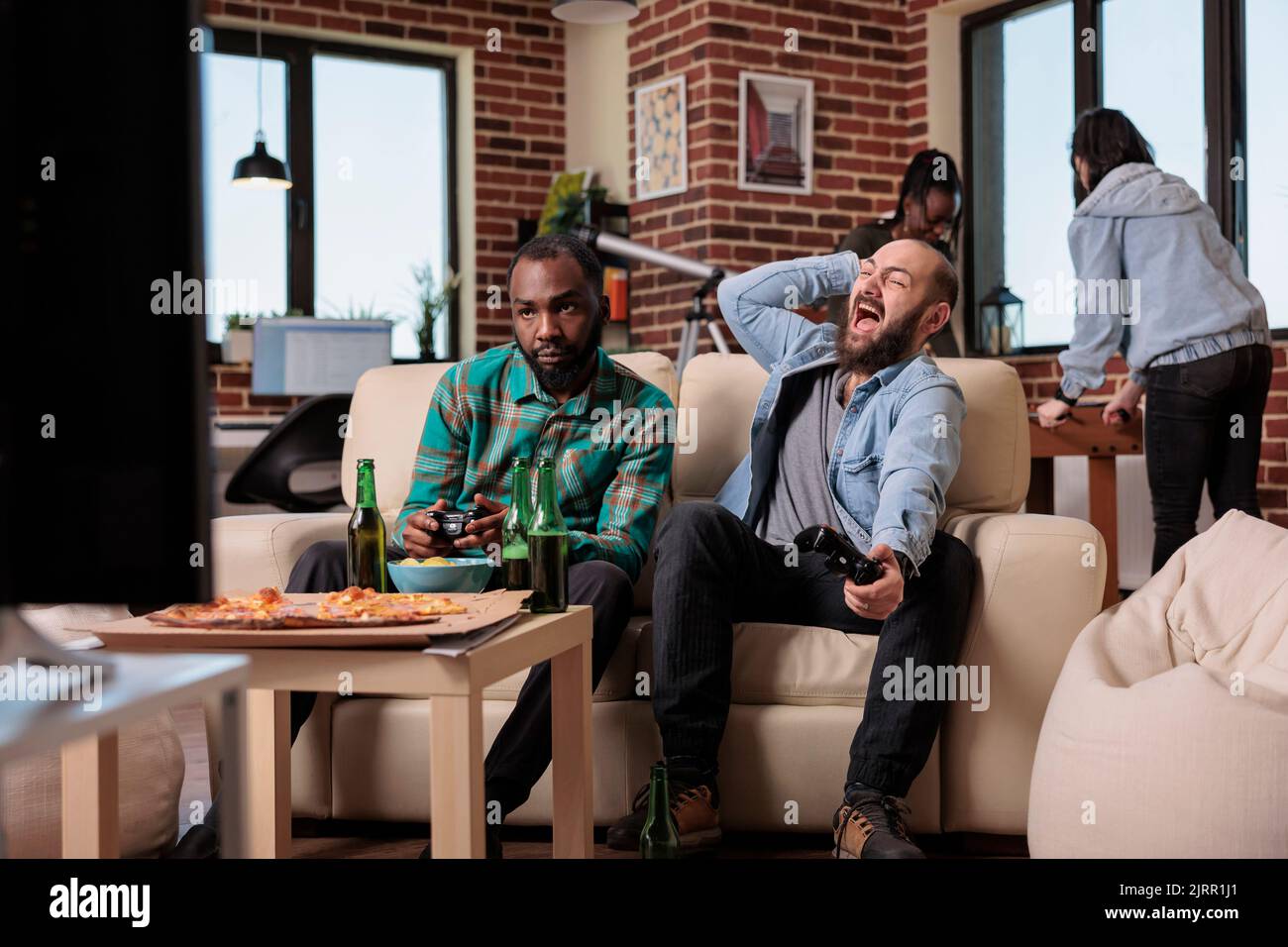 Frustrated men playing video games online and losing at home, feeling sad about lost competition. Group of friends enjoying fun leisure activity with alcohol beer bottles and food. Stock Photo