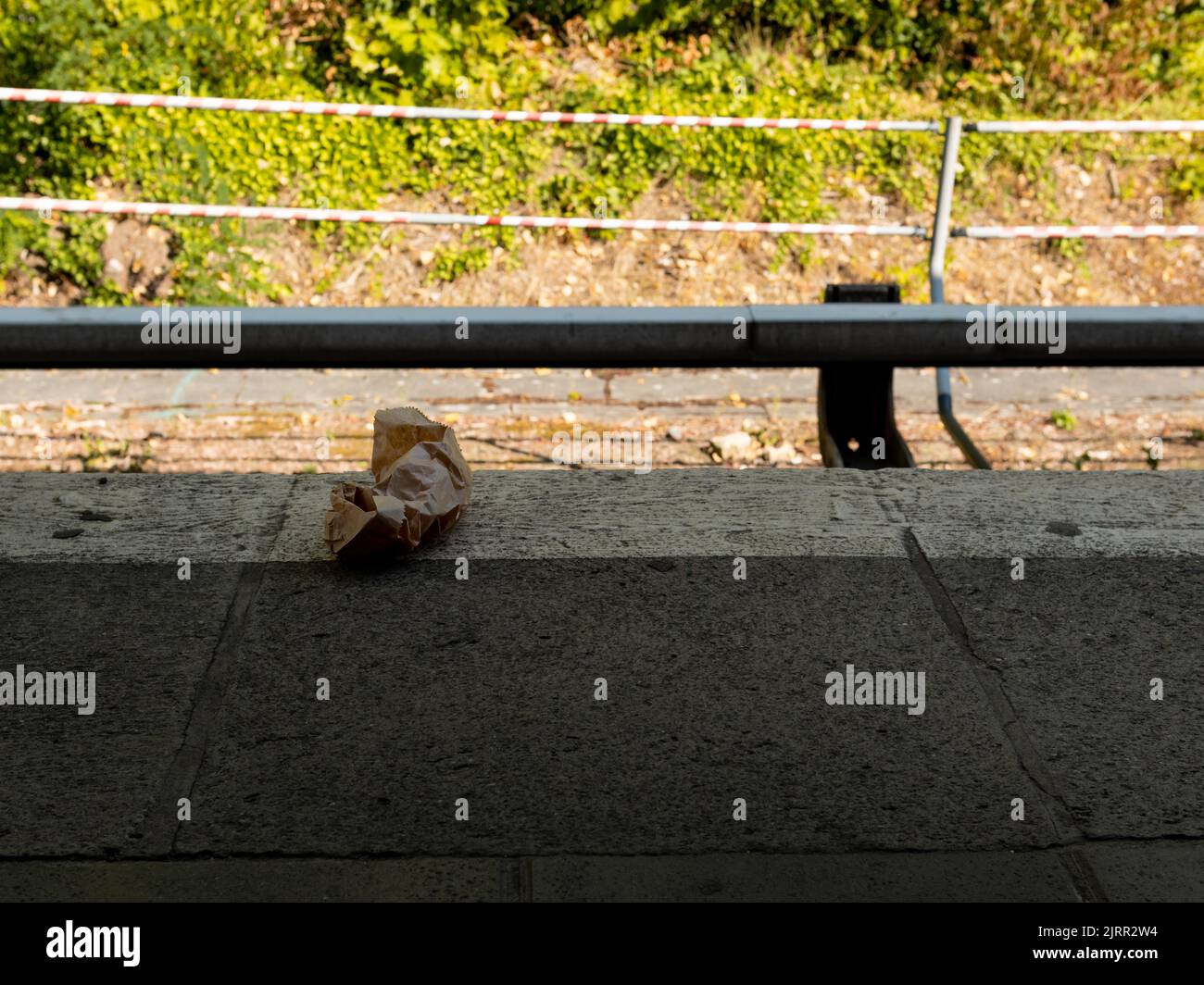 Waste at a train platform in the city. Rubbish lying on the ground. A dirty place at the public transportation facility. Thrown away paper trash. Stock Photo