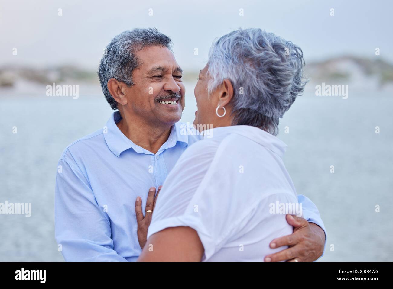 Senior, love and couple hug in nature at lake or beach on retirement holiday with a smile looking into eyes. Happy, romance and elderly man and woman Stock Photo