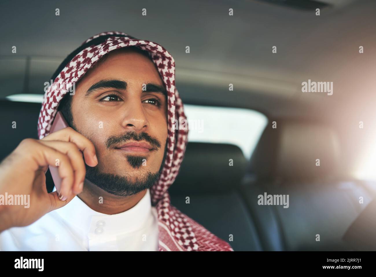 His expertise is always in demand. a young muslim businessman using his phone while traveling in a car. Stock Photo