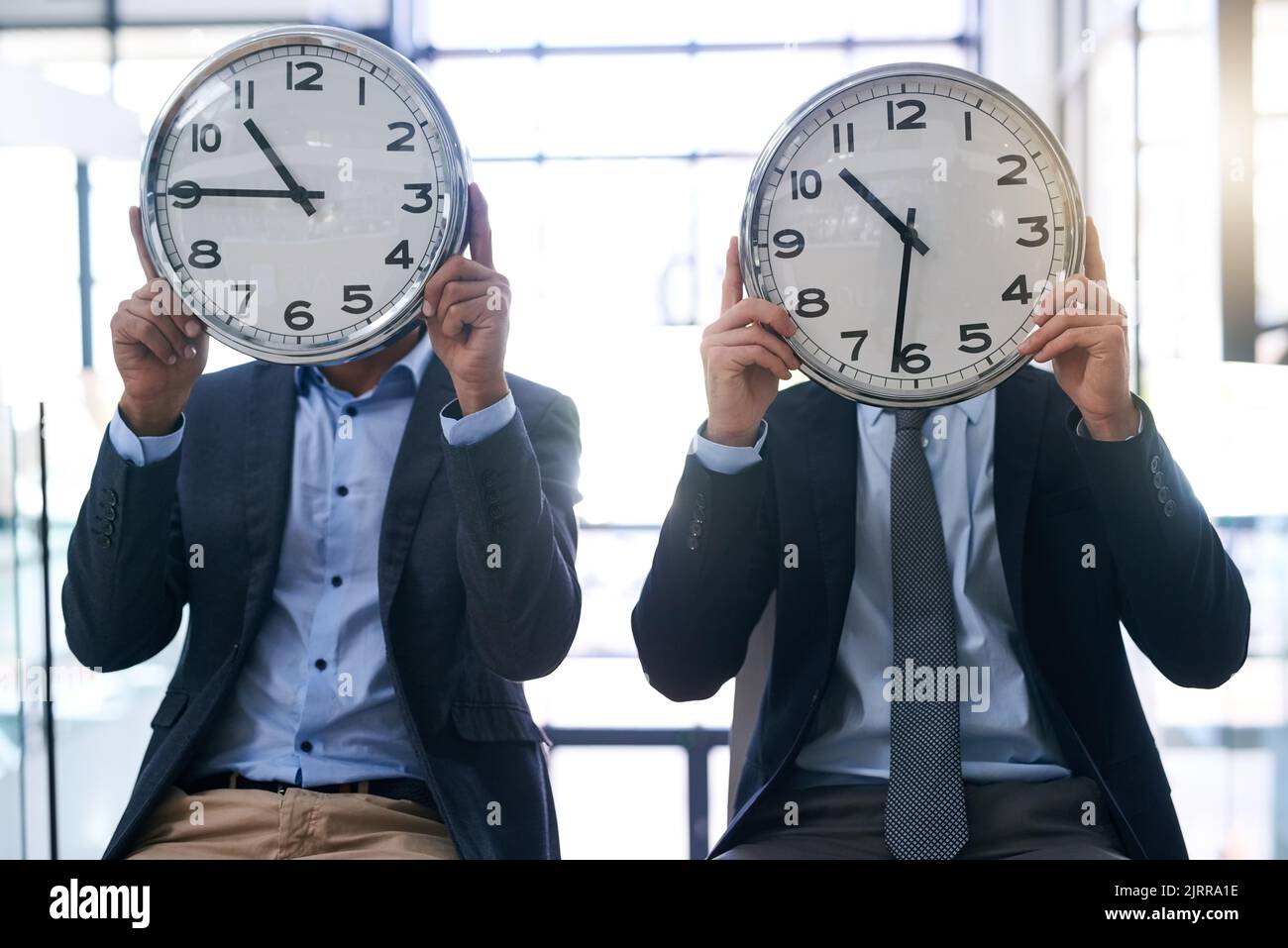 Times a wasting. two businessmen holding clocks over their faces in the