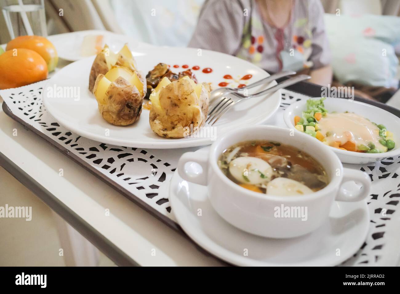 Female patient sitting on hospital bed having lack of appetite regardless varied and delicious meal on the table Stock Photo
