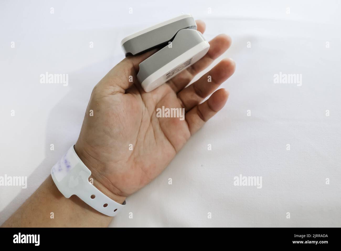 Patient on hospital bed using oximeter on thumb for measuring pulse and heart rate Stock Photo