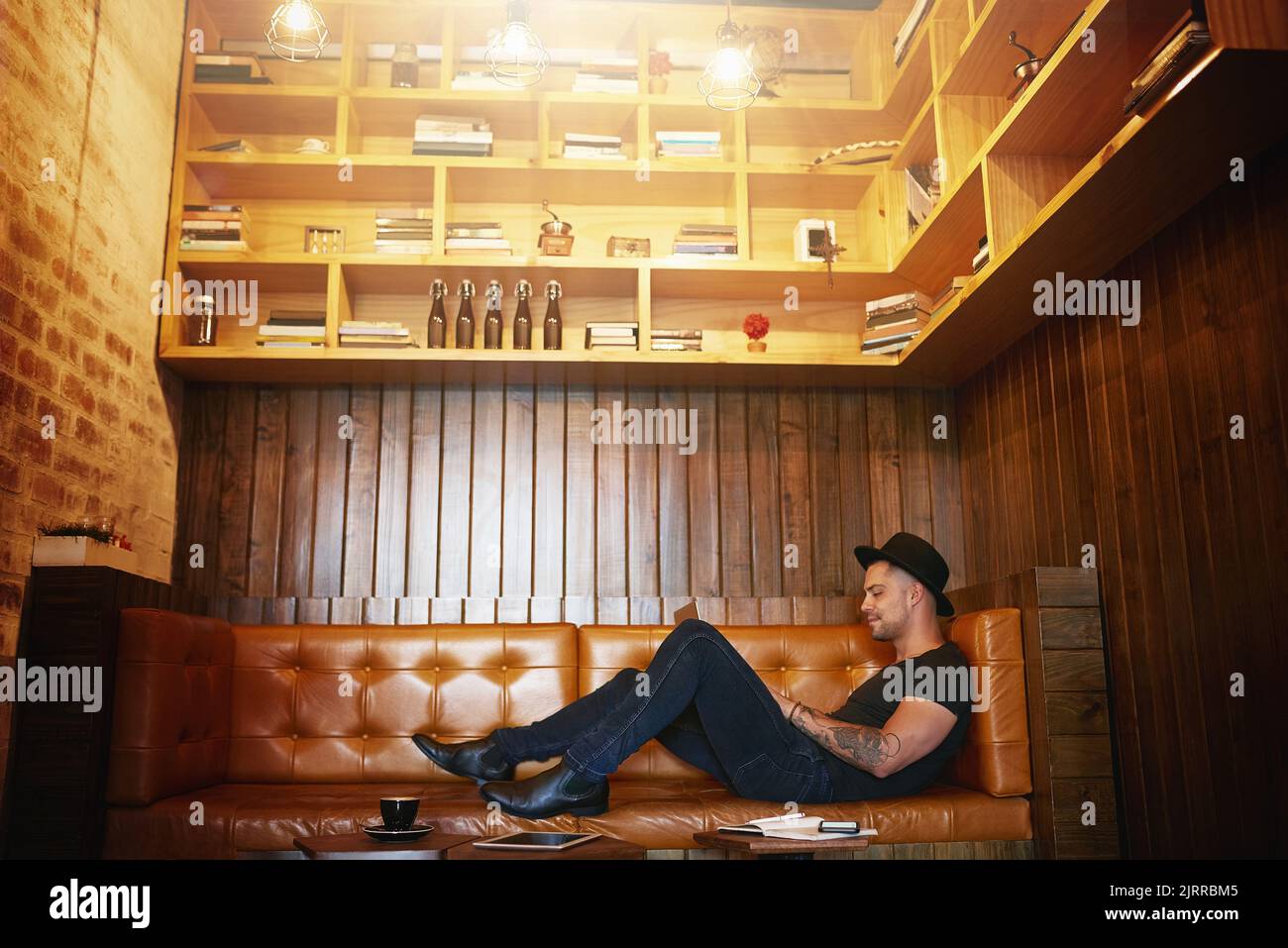 Relax and get work done Yes its possible. a handsome young man using a laptop on a sofa in a coffee shop. Stock Photo