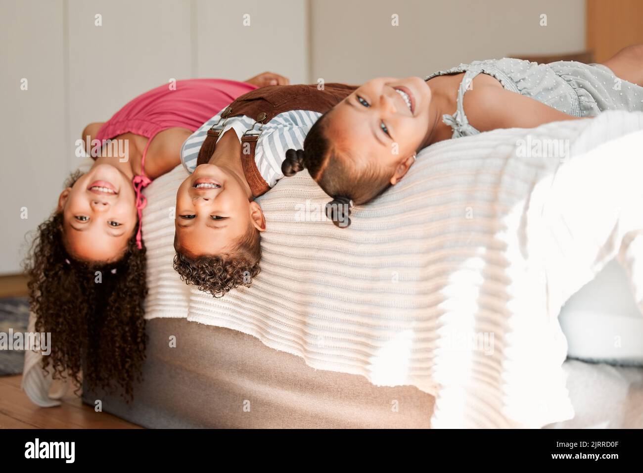 Fun, playful and silly kids lying on a bed with cute hairstyle and smiling portrait. Little siblings relaxing, playing indoors showing growth, child Stock Photo