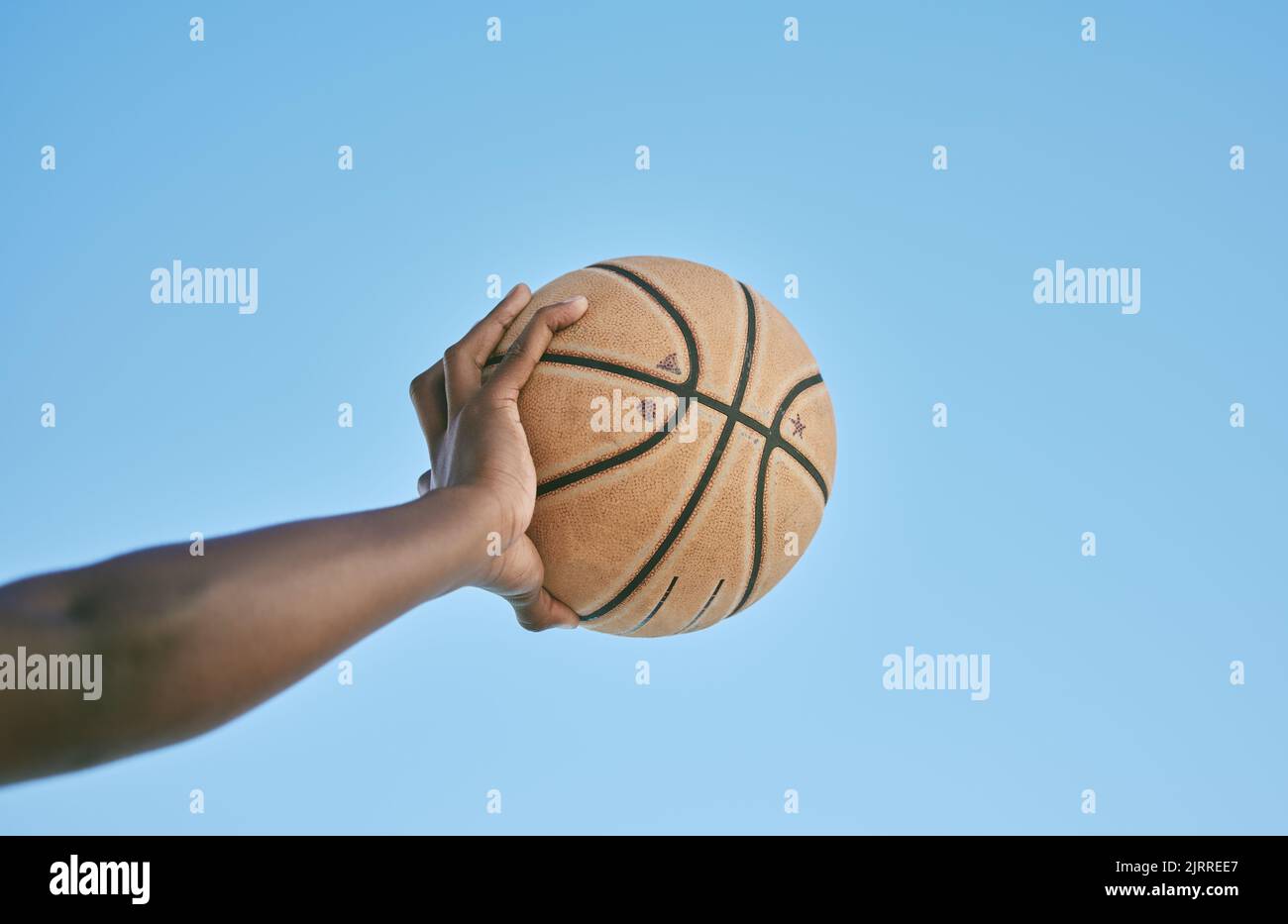 Basketball, active and sports man hand holding ball showing victory, power or athletic fitness from below with blue sky background. Player, black man Stock Photo