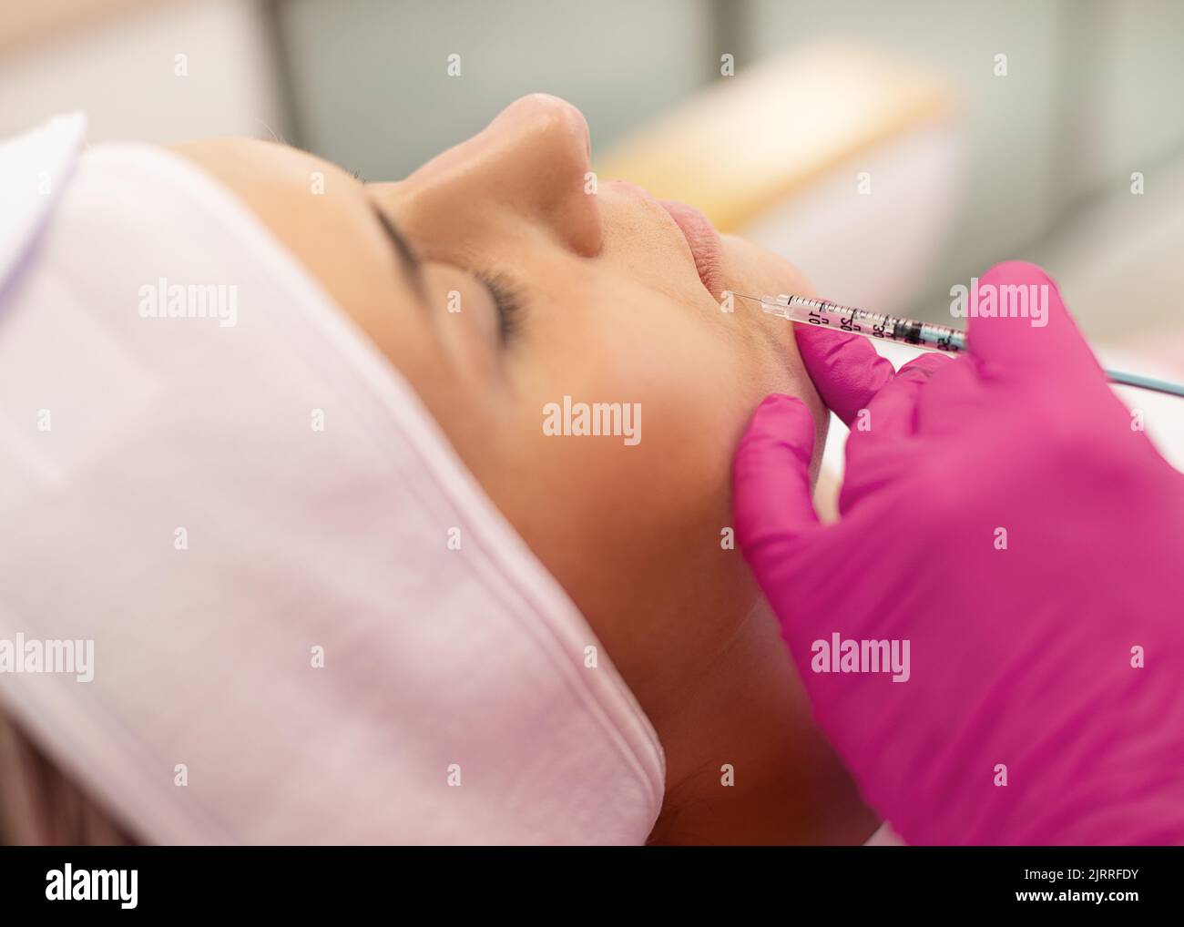 Side view of young woman getting beauty collagen injection. Cosmetologist making anti-wrinkle procedure in pink gloves. Stock Photo