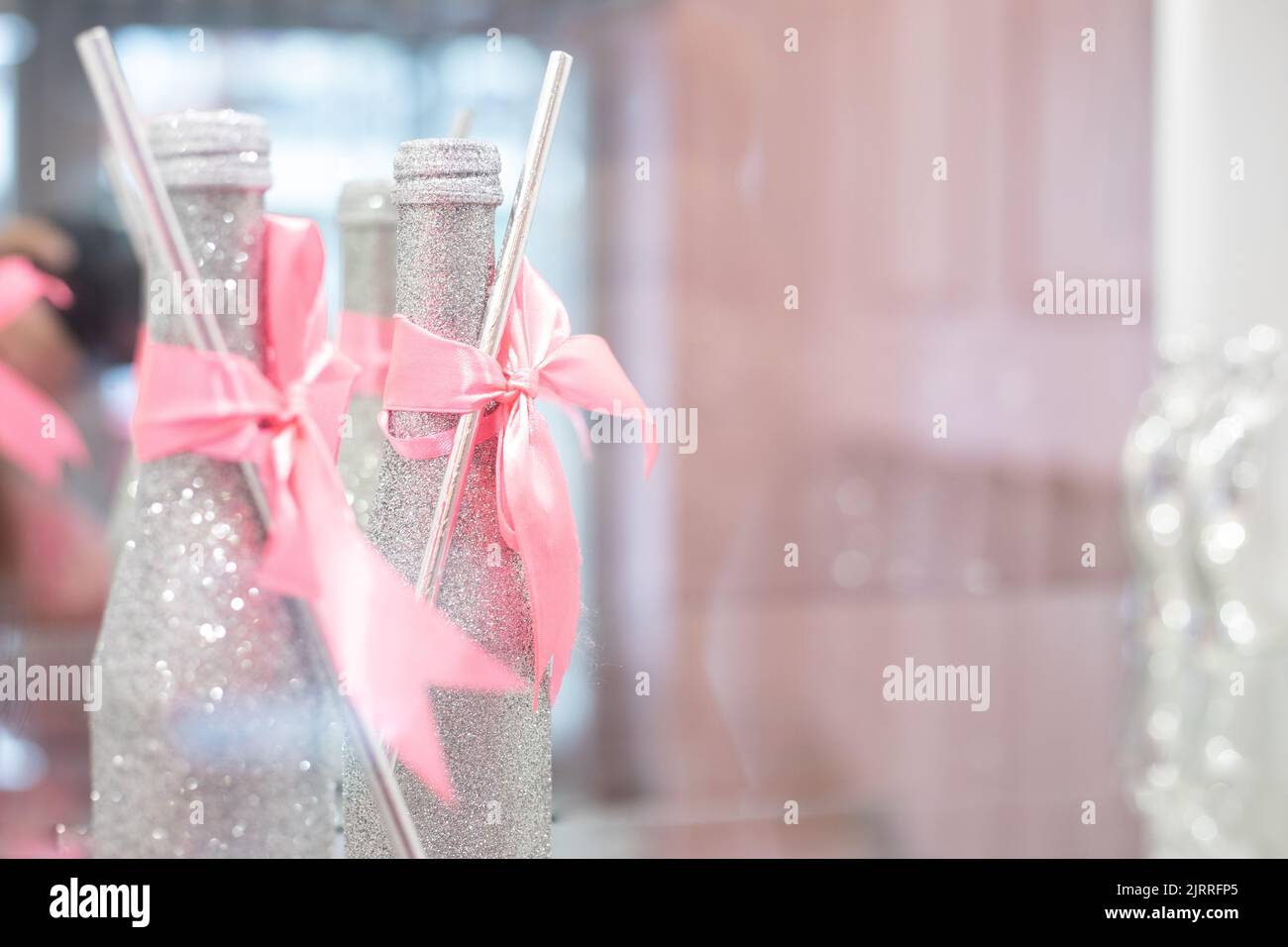 Festive serving of hall with decorated brilliant silver bottles of drink wrapped with pink ribbon and straw closeup. Decorations, event celebration Stock Photo
