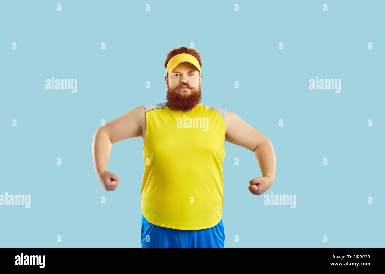 Funny serious fat man showing muscles after sports workout on light blue background. Stock Photo