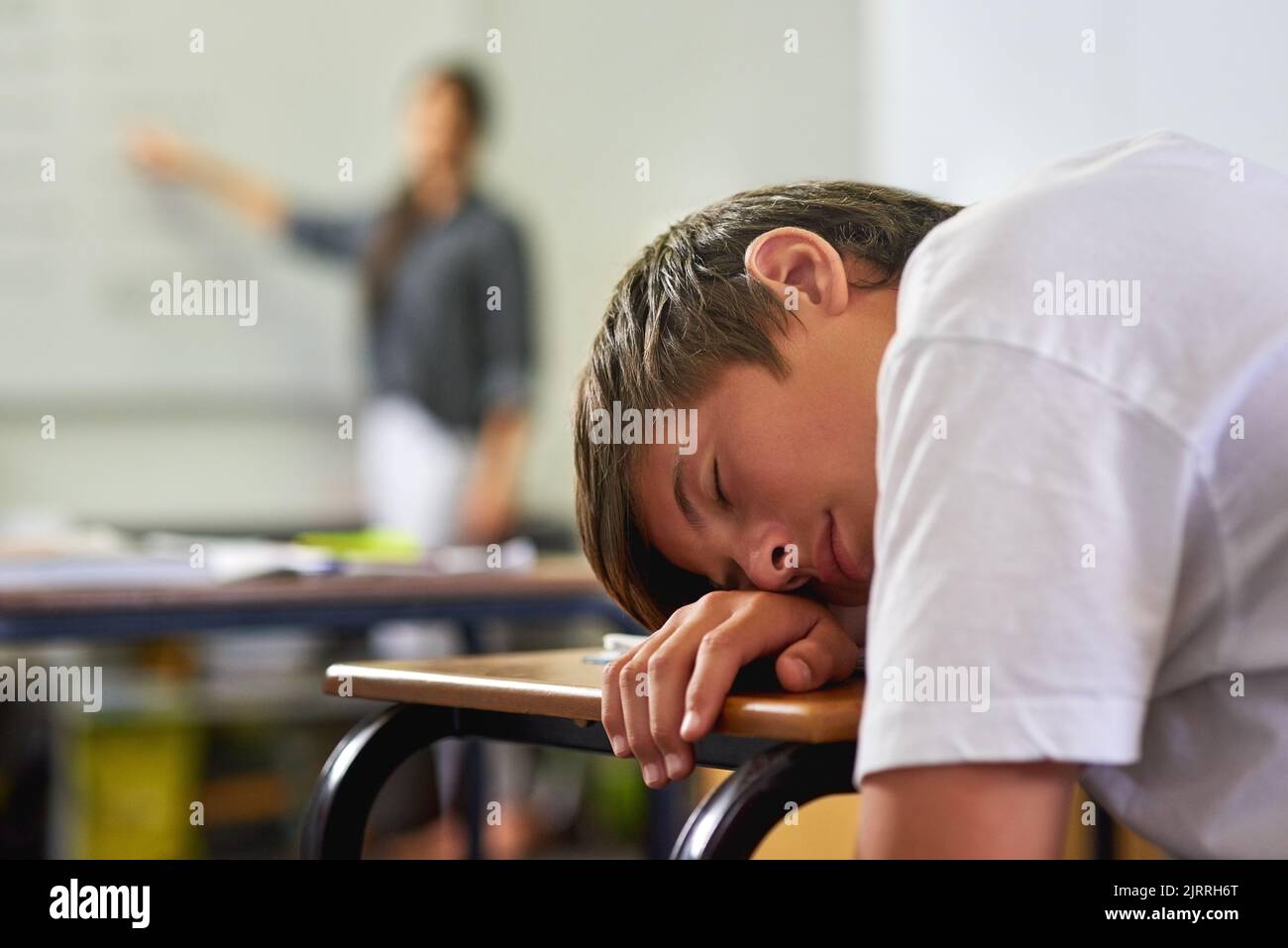 This class is a snoozefest. a young schoolboy sleeping on his desk in class. Stock Photo