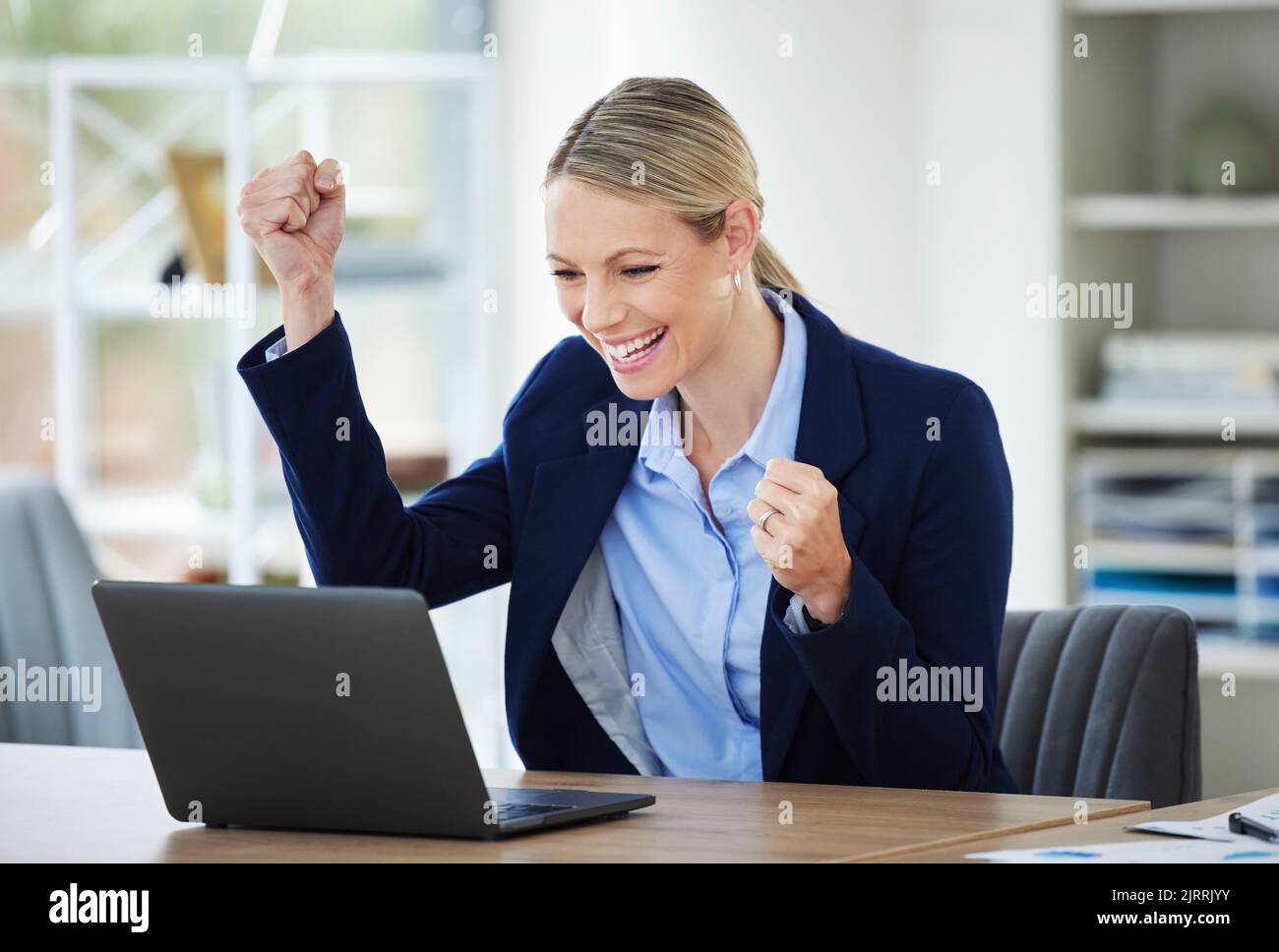 Happy and excited crypto winner celebrating stock market success while reading on laptop, winning and cheering for online bonus in an office Stock Photo