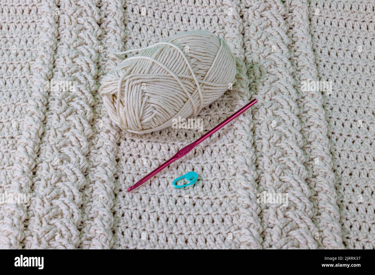 A cotton ball, pink metal hook and green stitch marker on a beige