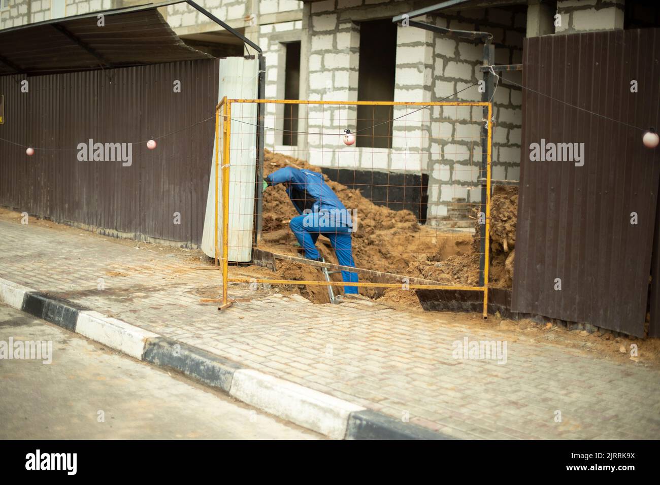 Worker near fence. Builder repairs house. Details of construction of house. Man on set. Stock Photo