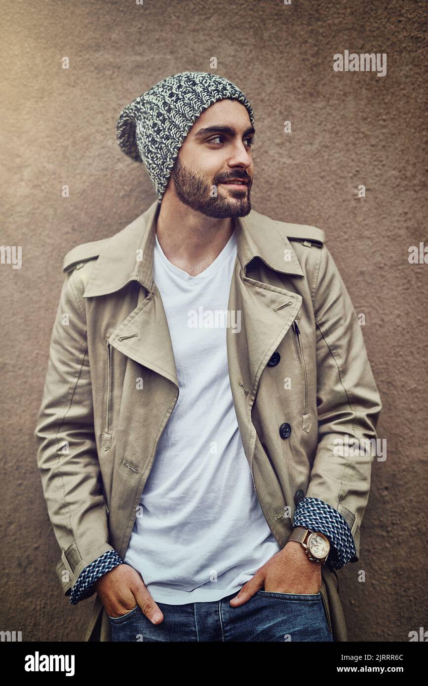 He gets his style inspiration from the streets. a fashionable young man wearing urban wear and posing against a brown wall. Stock Photo