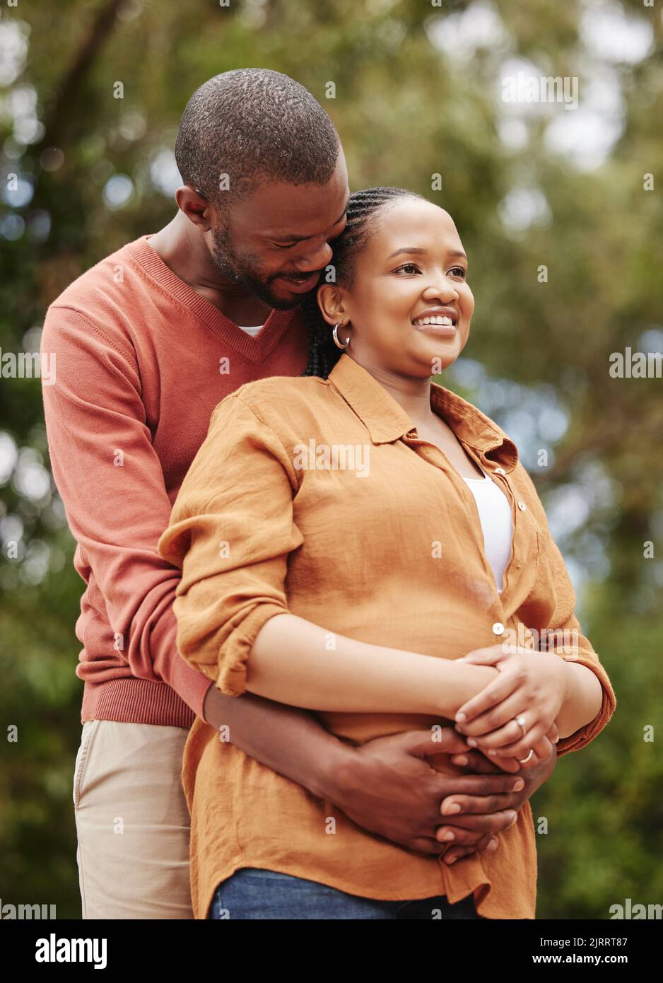 Romantic, loving and caring husband hugging his wife from the back in nature while on a date. Young, African and happy couple embracing each other Stock Photo