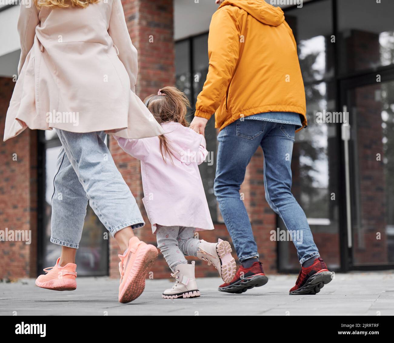 Back view of man and woman holding hands of little girl while walking down the street in new
